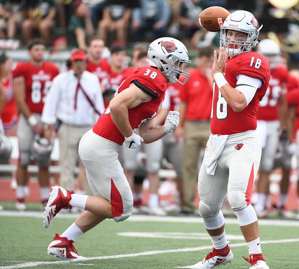 Johnny Davidson looks to throw a pass, with a running back in the background and coach Larry Kindbom deep in the background on the sidelines, out of focus. (Washington U. athletics photo by Danny Reise)